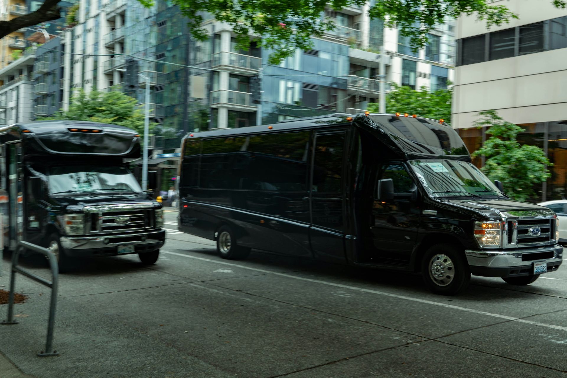 Two black buses driving on a city street.