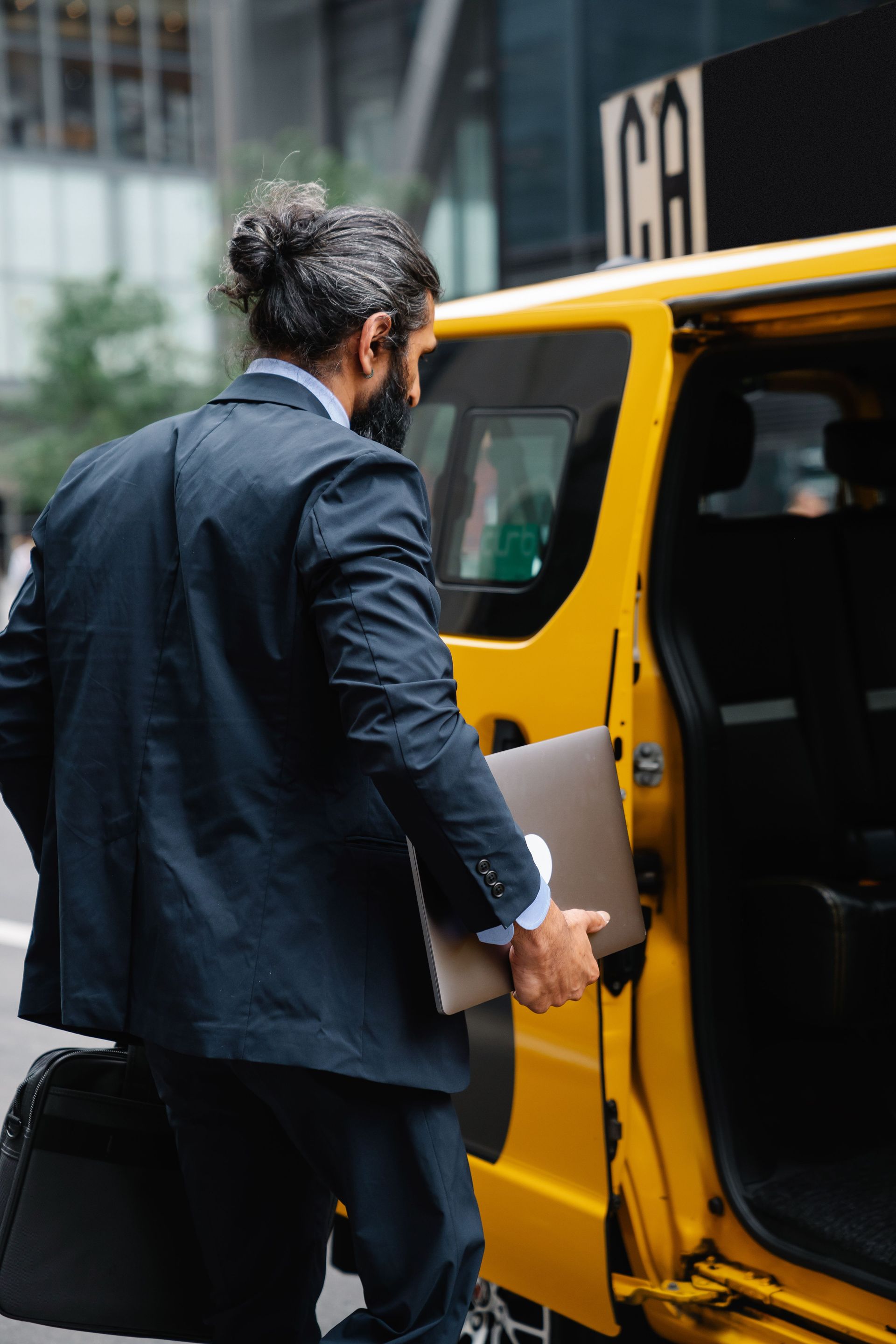 Professional man in formal wear entering a yellow taxi on a city street.