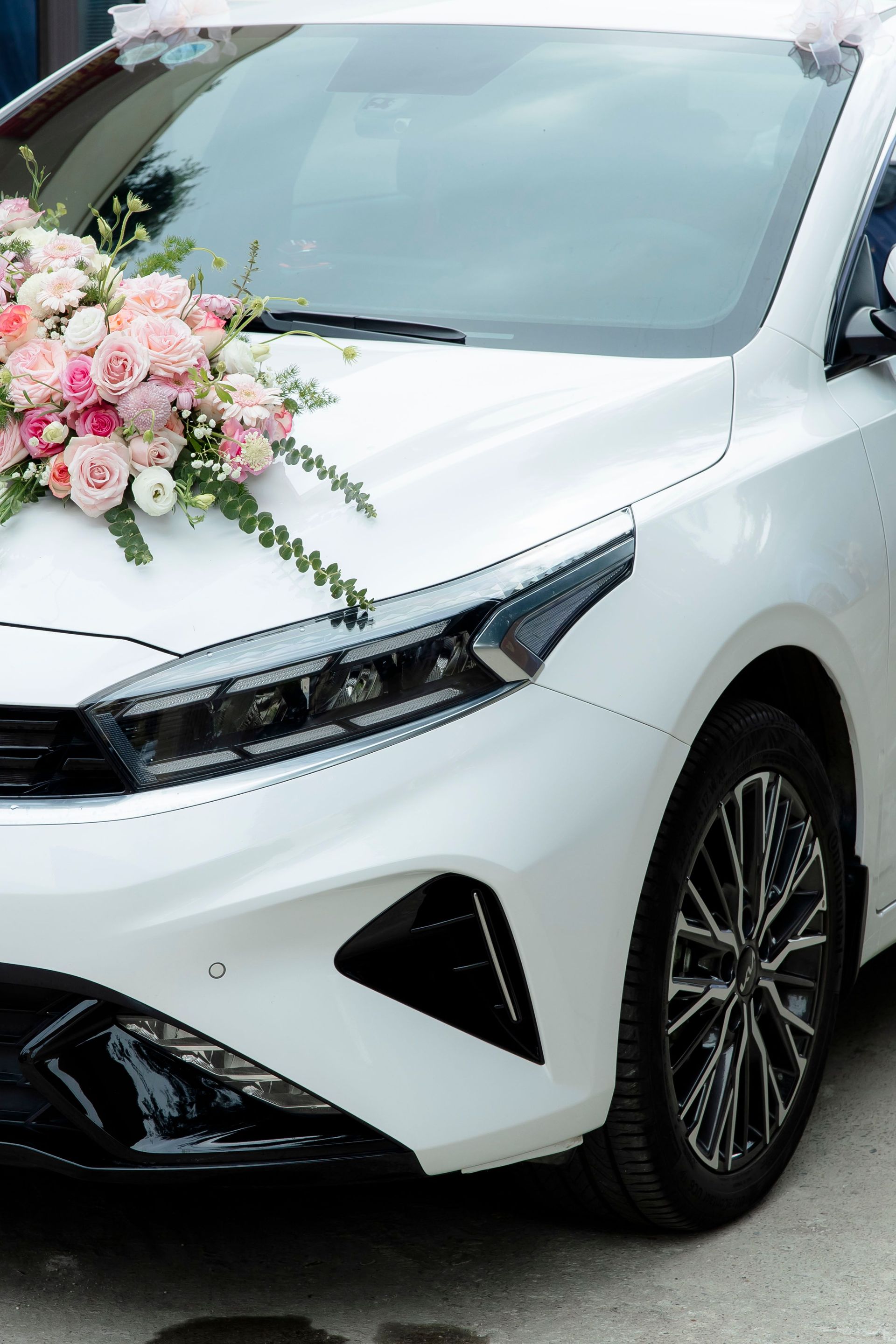 Close-up of a white car adorned with pink and white floral arrangement for a wedding ceremony.