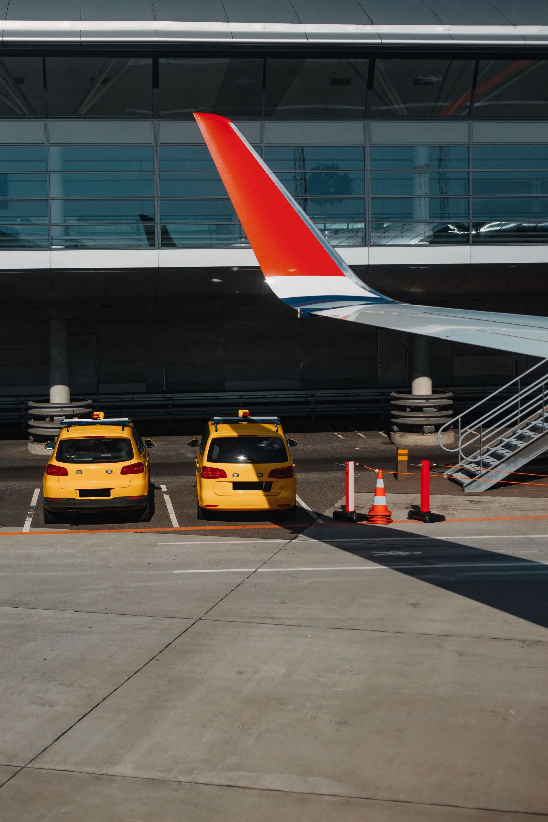 Two yellow taxis parked under an airplane wing at an urban airport.
